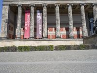 an outdoor stone walk in front of two columns in the building with flags and statues