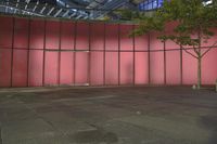 a red wall of a building with a tree in front of it and a person walking down the sidewalk beside the building