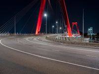 a long red bridge with a city in the background at night and cars driving under it