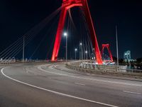 a long red bridge with a city in the background at night and cars driving under it