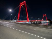 a long red bridge with a city in the background at night and cars driving under it