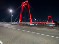 a long red bridge with a city in the background at night and cars driving under it