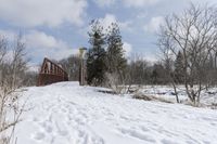 there is a red bridge in the middle of a snow covered field and some trees