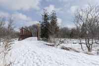 there is a red bridge in the middle of a snow covered field and some trees