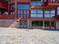 the view of the outside of a building with windows on all three floors, and people walking on stone pavement