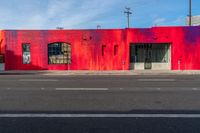 a red building with two windows painted on the side of it's front, near a street and a paved sidewalk