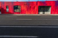 a red building with two windows painted on the side of it's front, near a street and a paved sidewalk