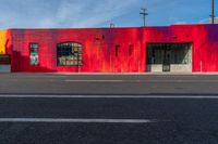 a red building with two windows painted on the side of it's front, near a street and a paved sidewalk