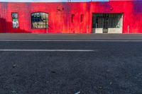 a red building with two windows painted on the side of it's front, near a street and a paved sidewalk