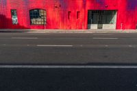 a red building with two windows painted on the side of it's front, near a street and a paved sidewalk