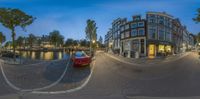 a picture of a red car on the street in front of buildings and water at dusk