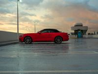 red car parked in an empty parking lot with a cloudy sky behind it, surrounded by a building