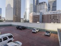 the red car is parked in the empty lot by the street with tall buildings behind it