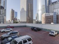 the red car is parked in the empty lot by the street with tall buildings behind it