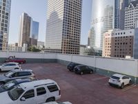 the red car is parked in the empty lot by the street with tall buildings behind it