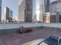 the red car is parked in the empty lot by the street with tall buildings behind it