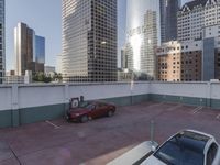 the red car is parked in the empty lot by the street with tall buildings behind it