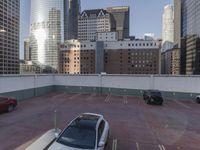 the red car is parked in the empty lot by the street with tall buildings behind it