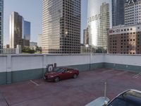 the red car is parked in the empty lot by the street with tall buildings behind it