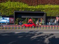 a red car parked in a parking lot next to tall green bushes and red traffic cones