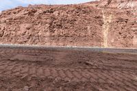 dirted mountain in front of a large red cliff in the desert of africa, with one dirted down road going in