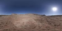 the panoramic photo shows a full moon over the red dirt hills near the intersection of a desert