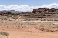 a red dirt road runs through a sandy landscape with rocks, scrubby hills and boulders