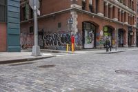 an empty bricked sidewalk in the city of new york city with a red fire hydrant and a brick building with a large doorway