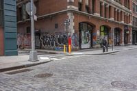 an empty bricked sidewalk in the city of new york city with a red fire hydrant and a brick building with a large doorway