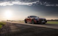 the red mercedes gt coupe is going down the road in front of the sun rays