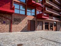 a red motorcycle parked next to a brick paved sidewalk and buildings that have balconies