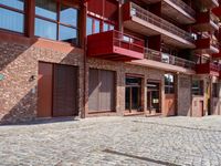 a red motorcycle parked next to a brick paved sidewalk and buildings that have balconies