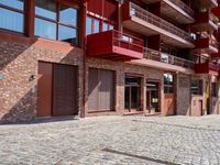 a red motorcycle parked next to a brick paved sidewalk and buildings that have balconies