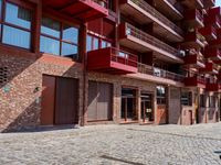 a red motorcycle parked next to a brick paved sidewalk and buildings that have balconies