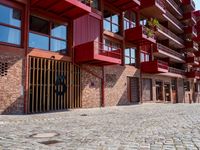 a red motorcycle parked next to a brick paved sidewalk and buildings that have balconies