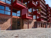 a red motorcycle parked next to a brick paved sidewalk and buildings that have balconies