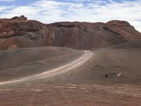 a red mountain in the middle of a desert with dirt roads passing through it with a lone horse walking away