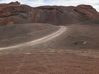 a red mountain in the middle of a desert with dirt roads passing through it with a lone horse walking away