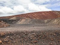 a red colored mountain with many rocks, gravel and dirt scattered in the ground below