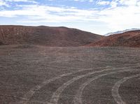 a big red mountain with tracks in the middle and dirt around it on the side of a hill