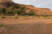 a large red mountain with a sign on it in the middle of nowhere area next to some brush and bushes