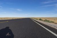 a single motorcycle rider and his shadow on a wide open road in the distance is the desert