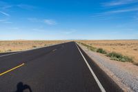 a single motorcycle rider and his shadow on a wide open road in the distance is the desert