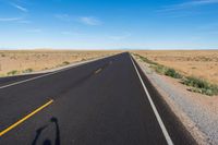 a single motorcycle rider and his shadow on a wide open road in the distance is the desert