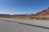 an empty street in the middle of a desert with mountains and sky behind it and in the foreground, a single motorcycle stands with the vehicle