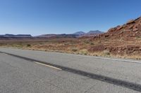 an empty street in the middle of a desert with mountains and sky behind it and in the foreground, a single motorcycle stands with the vehicle