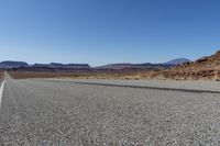 an empty street in the middle of a desert with mountains and sky behind it and in the foreground, a single motorcycle stands with the vehicle