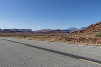 an empty street in the middle of a desert with mountains and sky behind it and in the foreground, a single motorcycle stands with the vehicle