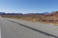 an empty street in the middle of a desert with mountains and sky behind it and in the foreground, a single motorcycle stands with the vehicle