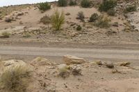 a dirt road with some rocks on the side and hills behind it is an area filled with rocks